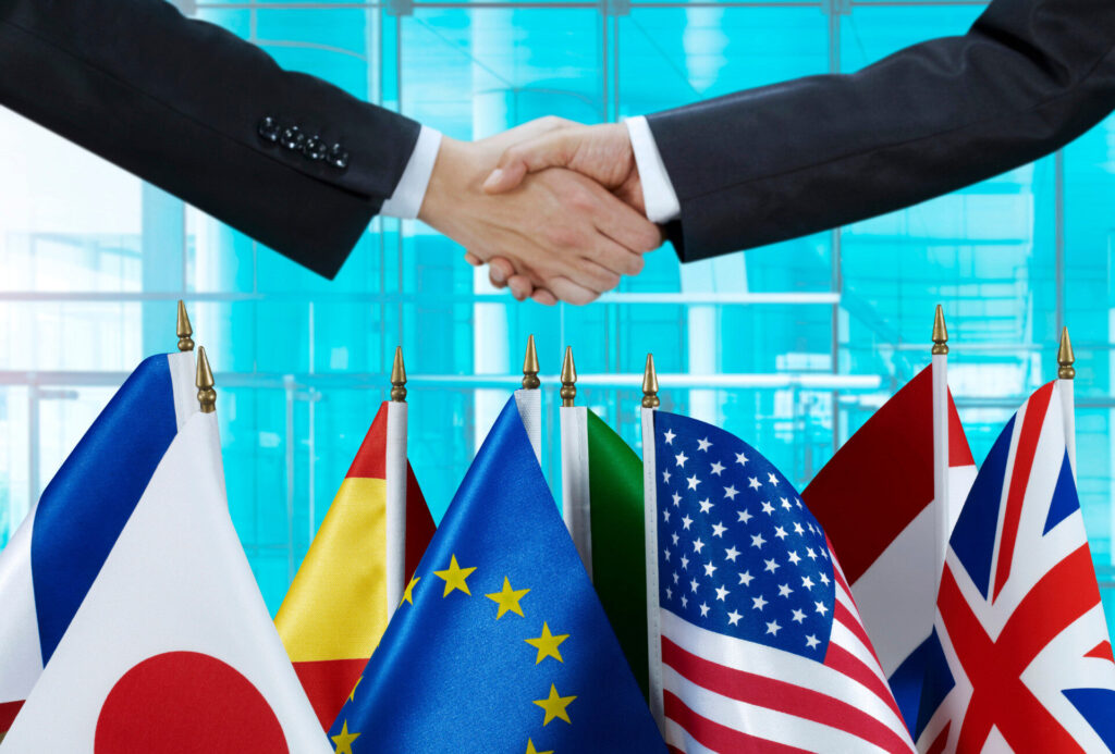 海外進出を目指す企業の国際ビジネス提携を象徴する握手と多国籍の国旗